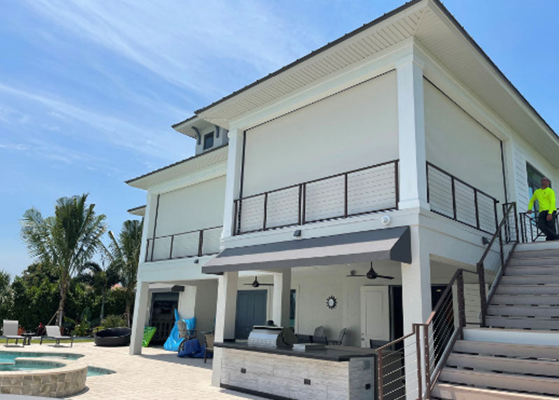 A waterfront home with a covered terrace and motorized screens on the lower level.